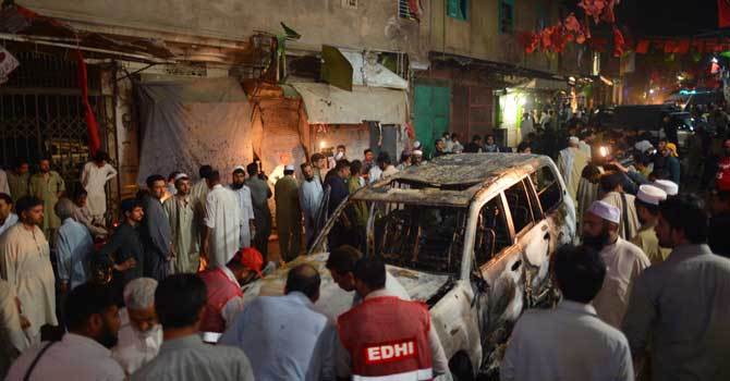Local residents and volunteers gather around a destroyed vehicle at the site of a suicide bomb attack at ANP's election campaign rally in Peshawar on April 16, 2013. —File Photo