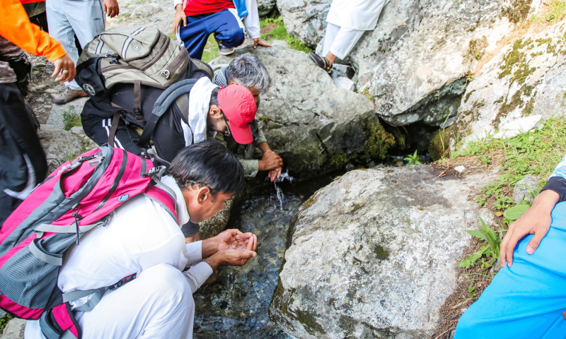 Visitors drink water from a cool spring on the way to Kamarkhwa twin waterfall in Mankiyal.