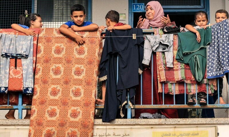 A woman and children stand before a mattress and laundry drying out on a balcony walkway outside a classroom that has been converted into a make-shift shelter for displaced Palestinians at a school run by UN. — AFP