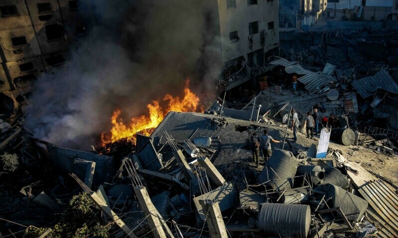 Palestinians stand on the rubble of a levelled building as smoke and fire rise from the destruction following an Israeli strike in Gaza City on October 26. &mdash; AFP