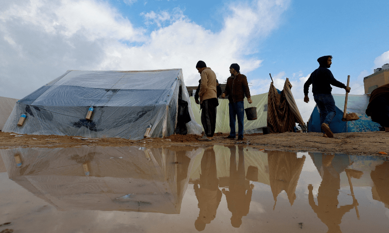  Displaced Palestinians walk next to tents following heavy rains at tent camps in Rafah in the southern Gaza Strip on Dec 13, 2023. &mdash; Reuters 