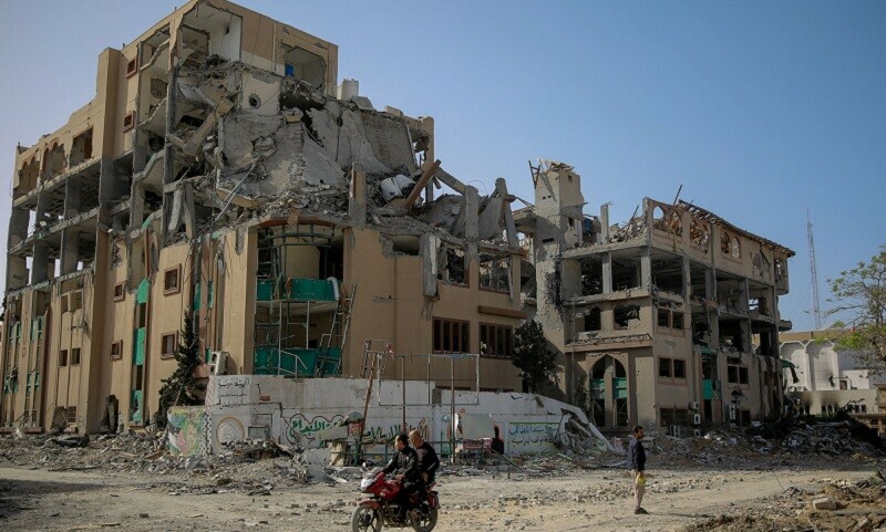 Palestinians drive a motorcycle past the destroyed building of the Islamic University in Gaza City on November 26, 2023. &mdash; AFP