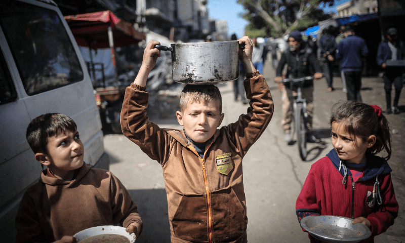 Children carry kitchen utensils as they walk toward a food distribution point in Khan Younis in the southern Gaza Strip on March 7, 2024. &mdash; AFP 