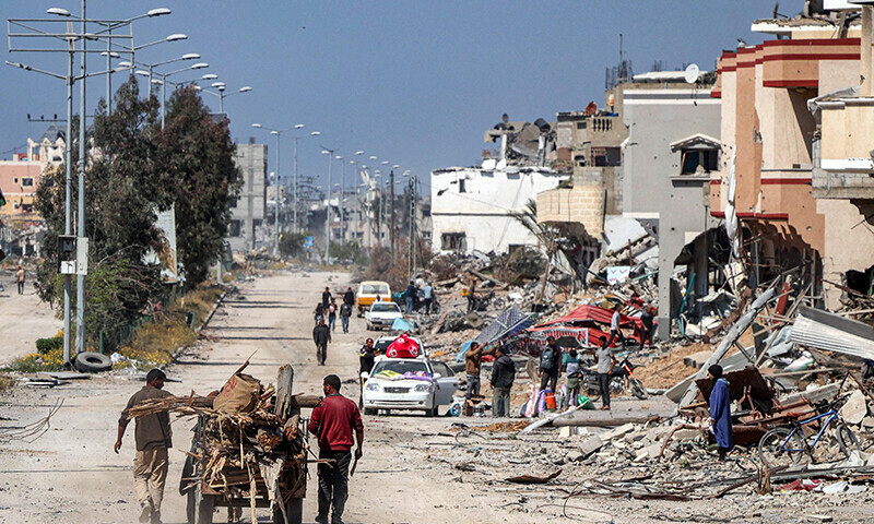 Men walk with an animal-drawn cart carrying salvaged wood from debris and trees past destroyed buildings in Khan Younis on April 7. &mdash; AFP
