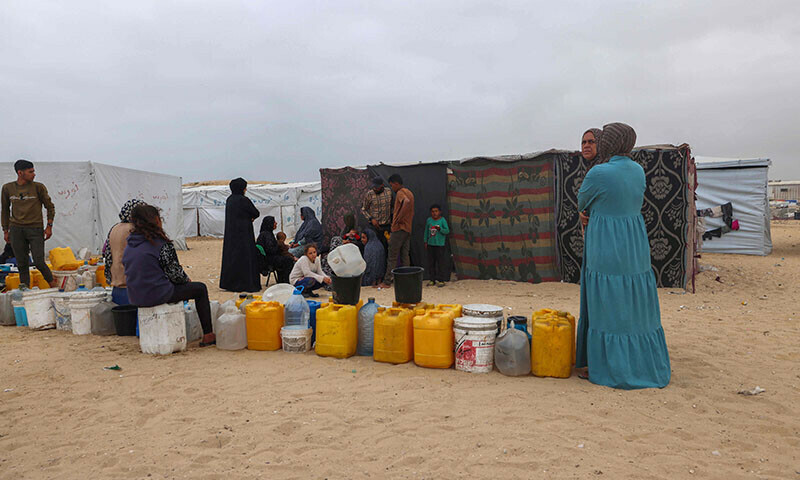 Displaced Palestinians wait by containers for water at a tent camp in Rafah on April 26. &mdash; AFP