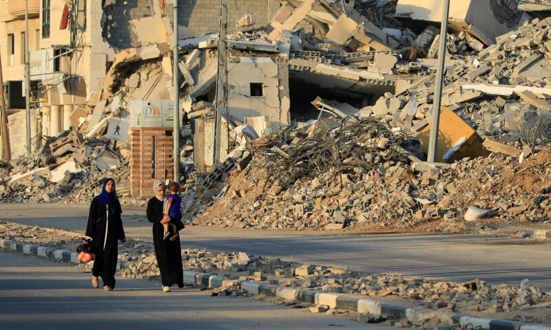  Displaced Palestinians walk past destroyed buildings in al-Bureij refugee camp in the central Gaza Strip on June 12, 2024. &mdash; AFP 