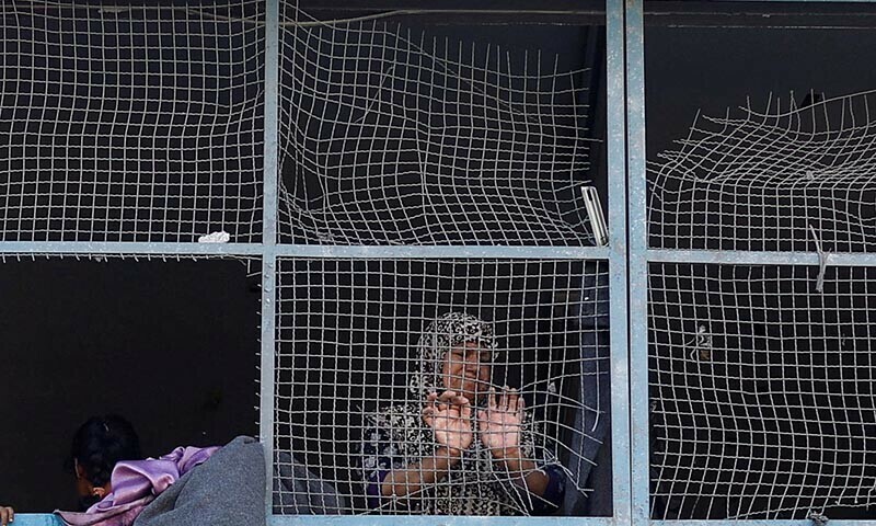 A Palestinian woman looks through the damaged windows of a classroom in a UNRWA school, after an air strike on a neighbouring house in Khan Younis on June 21. &mdash; Reuters