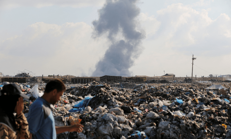  Palestinians walk as smoke rises following Israeli strikes in Hamad City, in Khan Younis in the southern Gaza Strip on Aug 11, 2024. &mdash; Reuters 