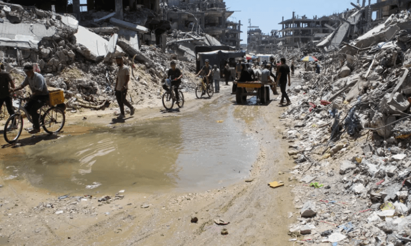 Palestinians make their way through a road with a puddle of wastewater as destroyed houses lie in ruins in Jabalia in the northern Gaza Strip on August 5. &mdash; Reuters