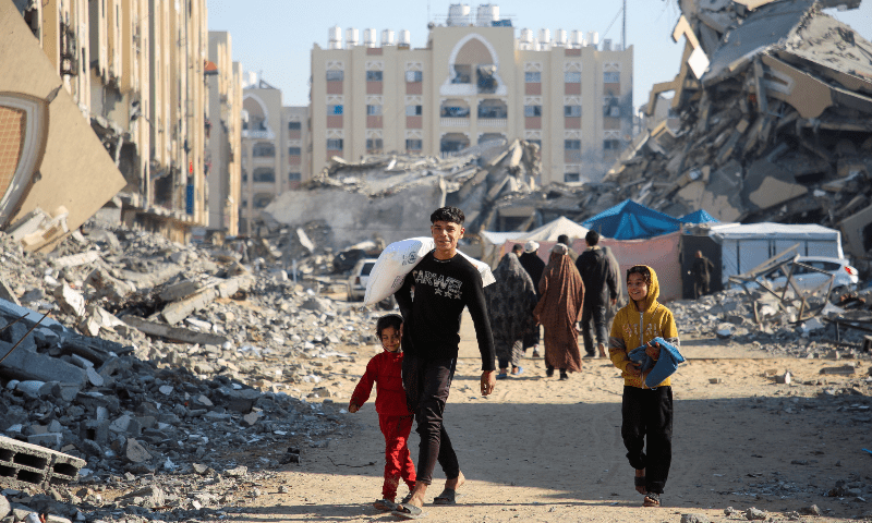  A Palestinian man walks past the rubble as he carries a bag of flour distributed by the United Nations Relief and Works Agency (UNRWA), in Khan Younis in the southern Gaza Strip on Dec 3, 2024. &mdash; Reuters 