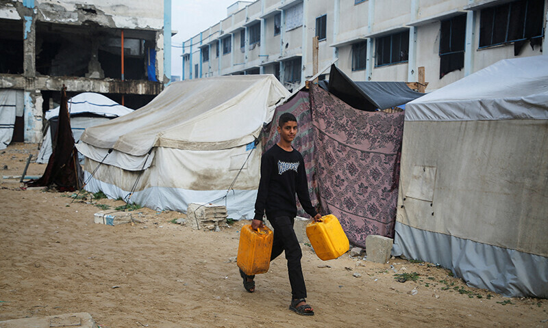 A Palestinian boy carrying plastic jerrycans walks past tents sheltering displaced Palestinians at a camp, ahead of a ceasefire set to take effect on Sunday, in Khan Younis in the southern Gaza Strip January 16. — Reuters