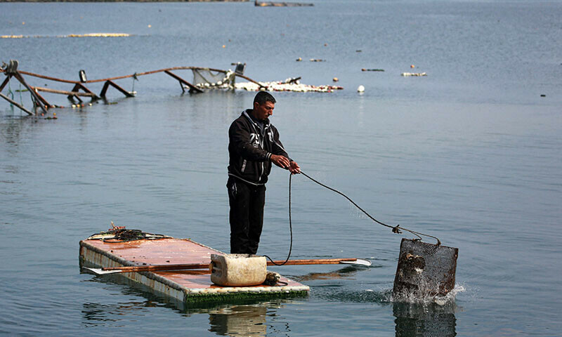 A Palestinian man stands on the door of a refrigerator that he uses as a makeshift rowing boat, as he throws his fishing basket into the sea at the port of Gaza City on March 9. — AFP