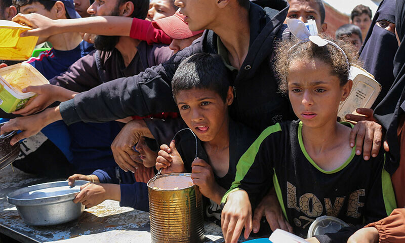 Palestinian children queue for a portion of hot food distributed by a charity kitchen at the Nuseirat refugee camp in the central Gaza Strip on May 5. — AFP