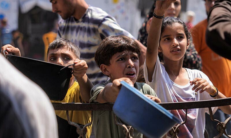 Children queue with pots to receive meals from a charity kitchen in Gaza City on July 14. — AFP