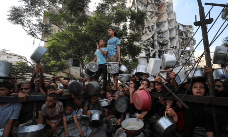  Palestinians wait to receive food from a charity kitchen, amid a hunger crisis, as a destroyed building stands in the background, in Gaza City on July 14, 2025. &mdash; Reuters 