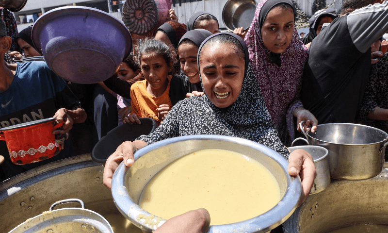 A displaced Palestinian girl reacts as she receives lentil soup at a food distribution point in Gaza City in the northern Gaza Strip on July 25, 2025. — Omar Al-Qattaa / AFP