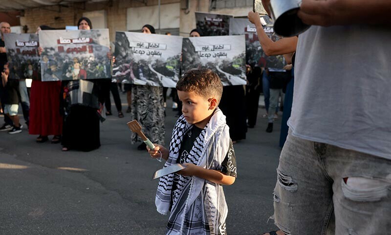 A boy bangs on a metal plate as Israeli Arabs hold placards on August 16, 2025, as they protest in the city of Lod near Tel Aviv, to denounce food shortages in the Gaza Strip and the ongoing war on the Palestinian territory. &mdash; AFP