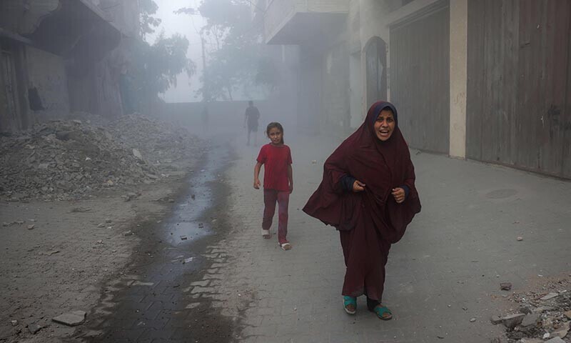 A Palestinian woman and children rush away from the site of Israeli air strikes on a six-storey building in the Saftawi neighborhood west of Jabalia in the northern Gaza Strip on August 19, 2025. &mdash; AFP
