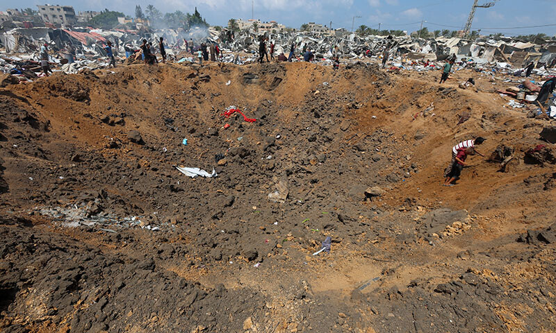 Palestinians stand next to a crater as they inspect the damage at the site of an Israeli strike on a tent camp sheltering displaced people, in Deir Al-Balah, in the central Gaza Strip on August 21. — Reuters