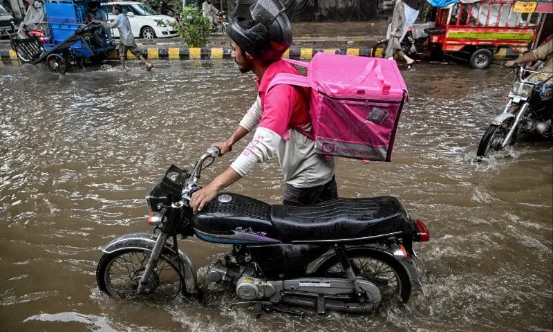 In this photograph taken on August 30, 2025, Abdullah Abbas, a food delivery rider for the Singapore-based company Foodpanda, pushes his bike through a flooded street after heavy rainfall in Lahore.  — AFP/ Aamir Qureshi