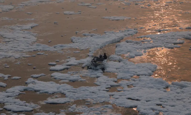 A man moves his boat through foam on the polluted Yamuna river, on a smoggy morning amid ongoing air pollution in New Delhi, India, on November 21. — Reuters
