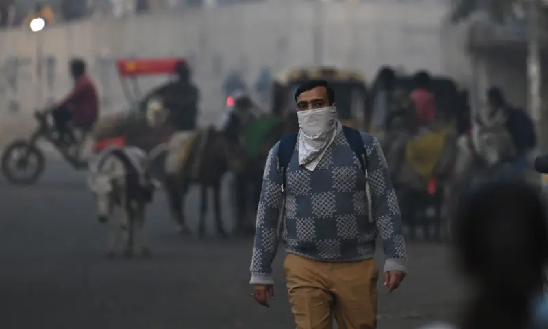 A man covering his face with a handkerchief walks along a road amid smoggy conditions in New Delhi on November 21. — AFP