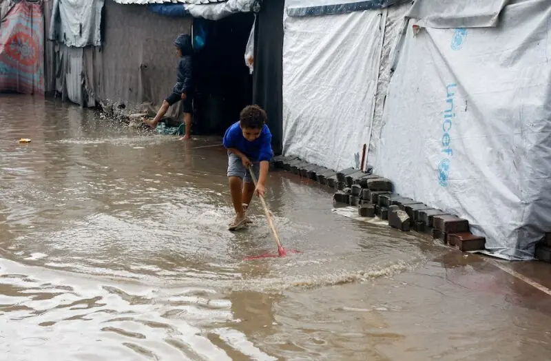 Displaced Palestinian children stand in flood water as they shelter at a flooded tent camp, during a rainy day in Gaza City, November 25. &mdash; Reuters
