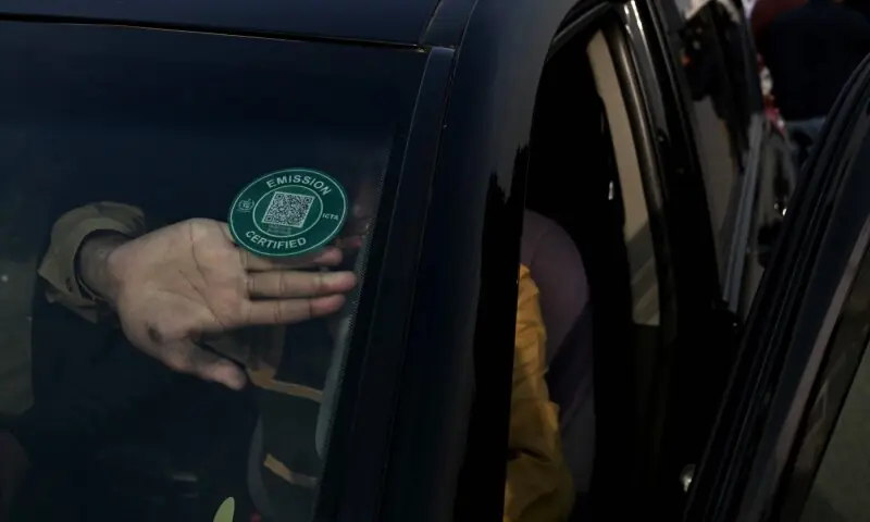 This picture taken on December 10, 2025, shows a technician pasting a certified sticker on a car after it cleared an emission test in Islamabad. &mdash; AFP