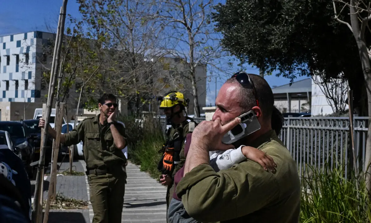 An Israeli soldier speaks on the phone while holding his child during the partial evacuation of a residential building damaged by shrapnel, after missiles were launched towards Israel from Iran following strikes by Israel and the U.S. on Iran, in Haifa, northern Israel on February 28, 2026. &mdash; Reuters