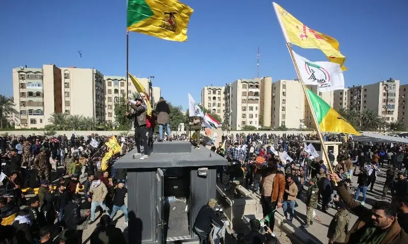  Protesters wave flags outside the US embassy in Baghdad. &mdash; AFP 