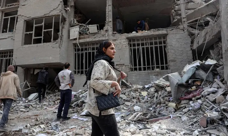 A woman stands in front of a destroyed residential building as residents collect their belongings from the rubble in Tehran on March 12, &mdash; AFP