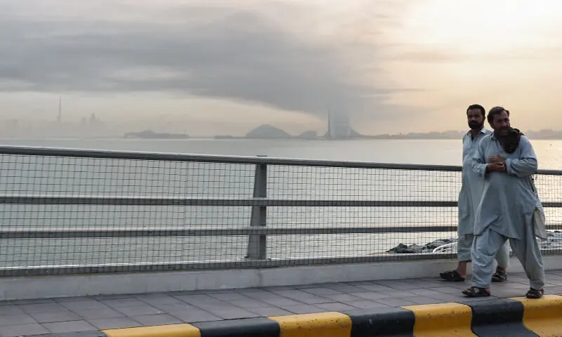 Men walk along a road as smoke is seen above Dubai on March 13, 2026. &mdash; AFP