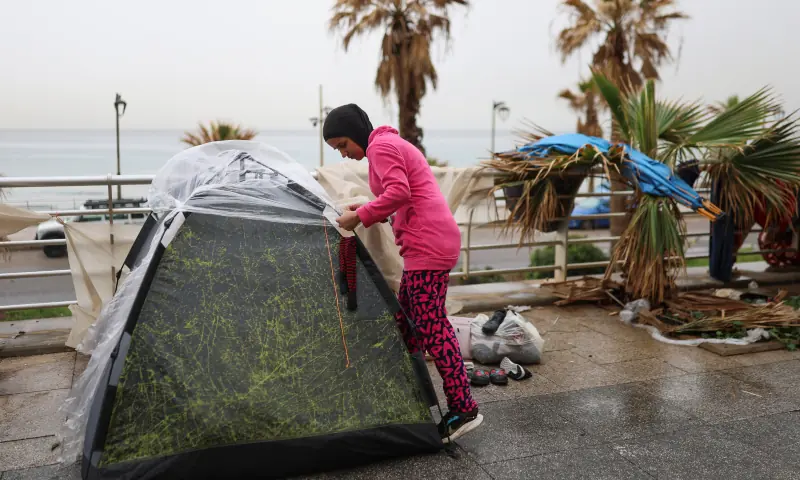 A woman covers their family&rsquo;s tent from the rain, as they have been living on a street along the corniche overlooking the sea, in Beirut, Lebanon on March 14, 2026. &mdash; Reuters