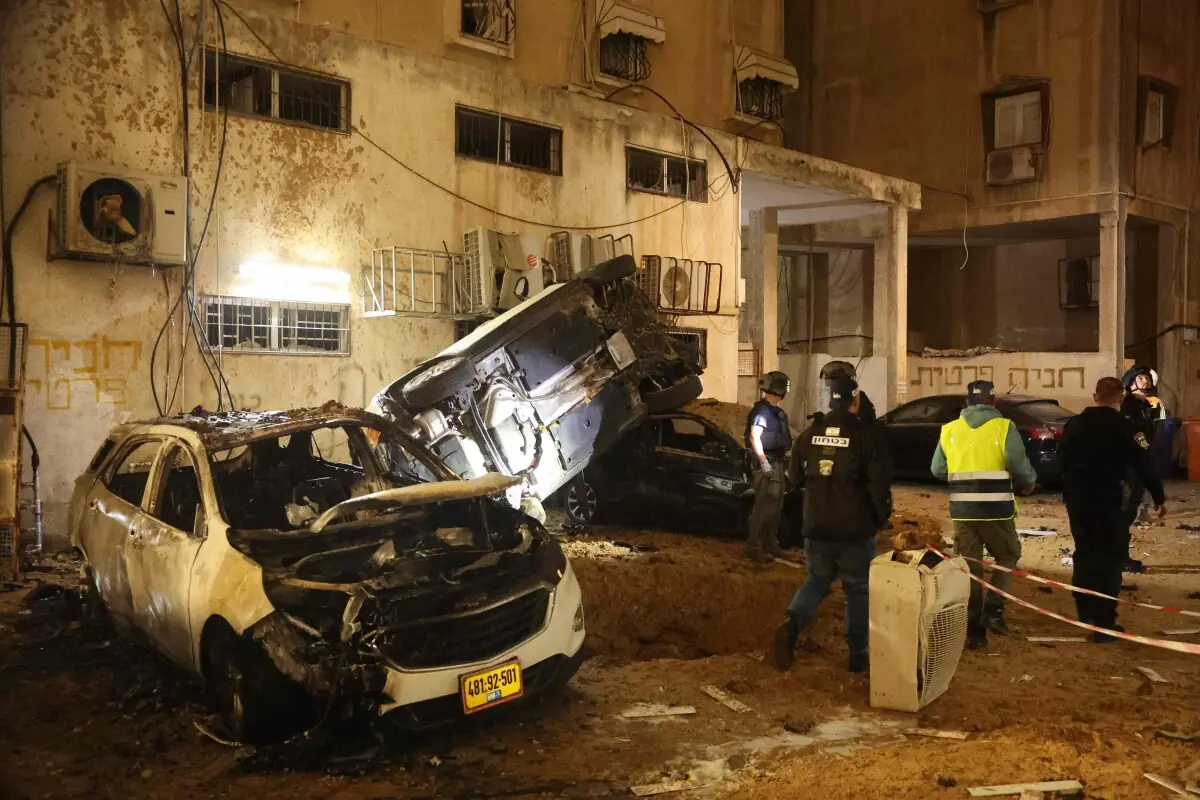 Israeli security checks the damage to cars after a rocket strike in Holon, Israel, on March 15, 2026. &mdash; AFP