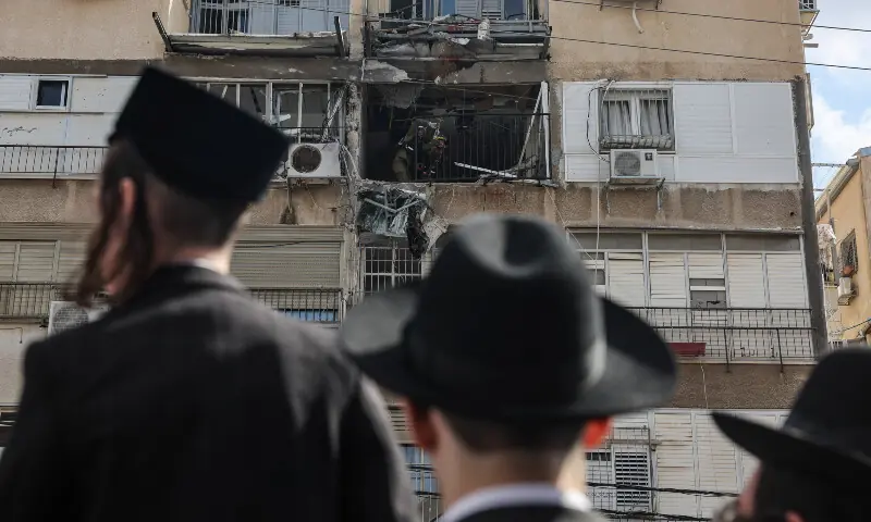 Ultra-Orthodox Jewish people gather outside a damaged building following an Iranian projectile strike, in central Israel on March 15, 2026. &mdash; Reuters