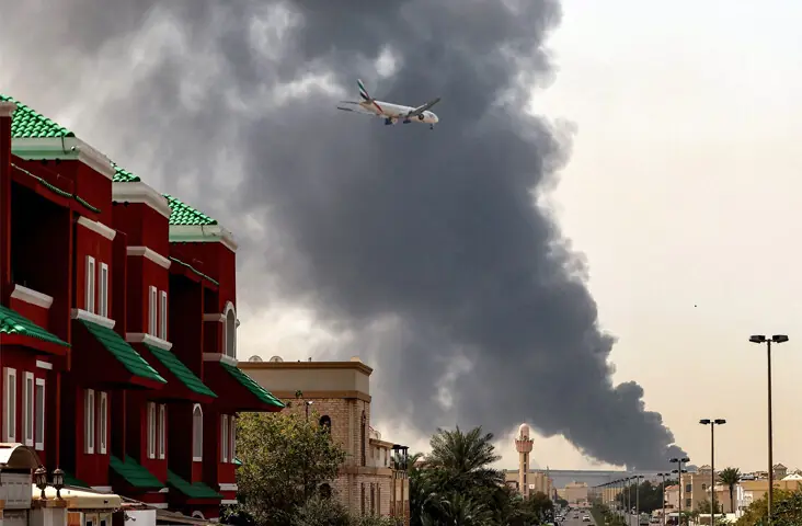  An Emirates aircraft prepares for landing as a plume of smoke rises from a fire near Dubai International Airport, following an Iranian attack.&mdash;AFP 