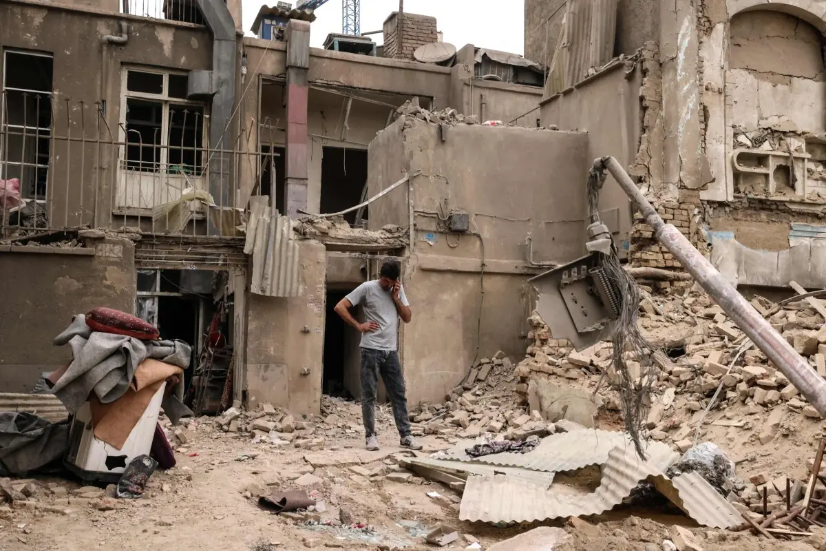 A man speaks on a mobile phone as he stands outside damaged homes, following a military strike on the Iranian capital Tehran on March 15, 2026. &mdash; AFP