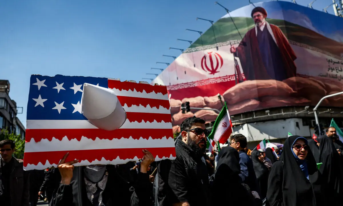 A person holds a placard representing a US flag, with an image of Iran’s new Supreme Leader Mojtaba Khamenei on a billboard in the background, on the day of a ceremony marking 40 days since Ayatollah Ali Khamenei was killed in Israeli and US strikes, in Tehran, Iran on April 9, 2026. — WANA via Reuters