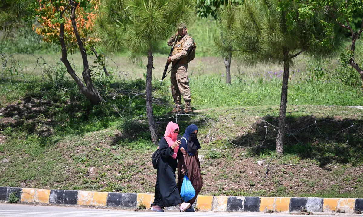 Women walk past a Pakistani army personnel standing guard in the Red Zone area in Islamabad on April 9, 2026. &mdash; AFP