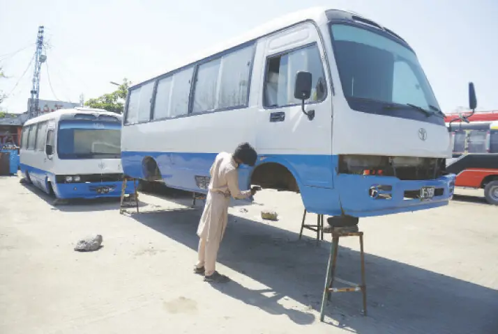   A mechanic repairs a vehicle at a workshop set up along the bus stand.  