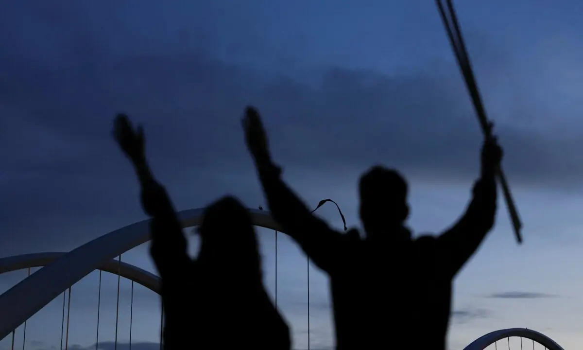 People gesture as anti-war protester Guido Reichstadter sits atop the Frederick Douglass Memorial Bridge in Washington, DC, US on May 5, 2026. &mdash;Reuters
