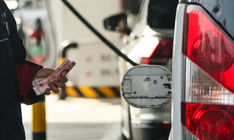 An employee holds Chinese Yuan notes next to an open cap of a car&rsquo;s fuel tank at a gas station ahead of an announced fuel price hike, amid the US-Israeli war on Iran, in Beijing, China on March 22, 2026. &mdash; Reuters/File