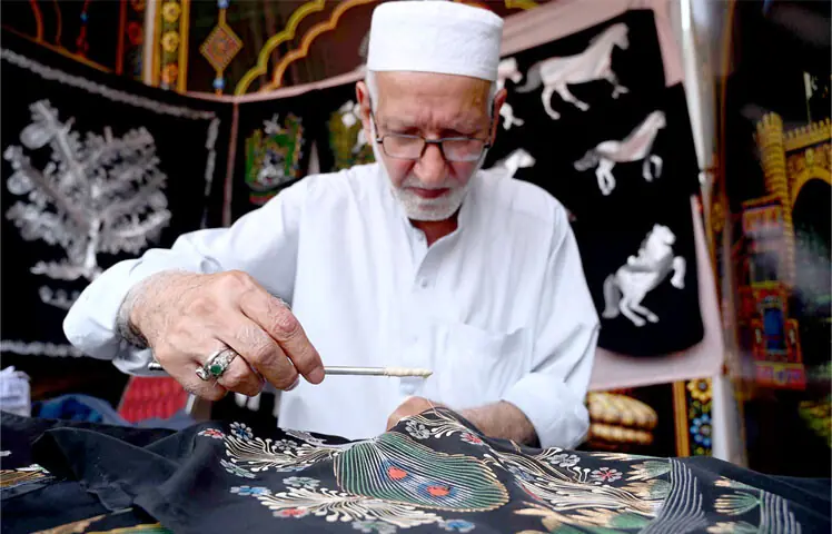  A craftsman uses wax art technique to draw an intricate design on a piece of fabric during Hunar Mela at Nishtar Hall, Peshawar, on Friday. &mdash; APP 