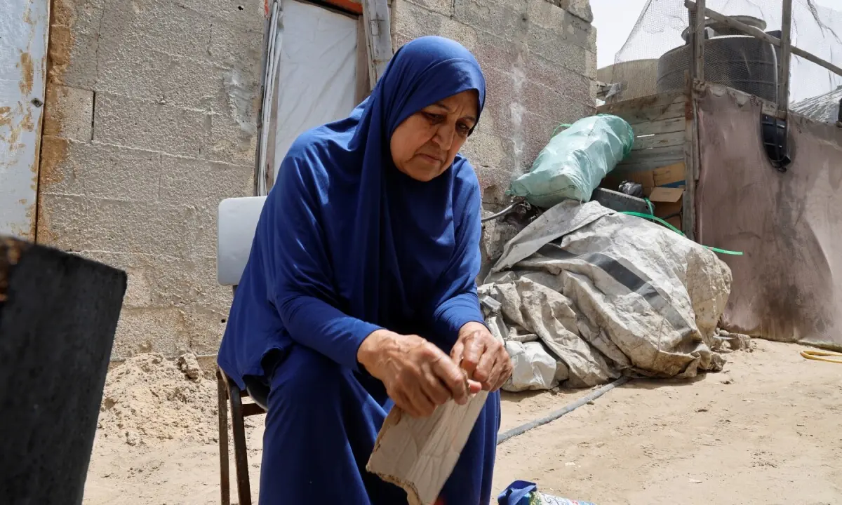 Palestinian Najia Abu Lehia sits outside a tent at a camp for displaced people in Khan Younis, lighting a fire on May 18, 2026. —REUTERS