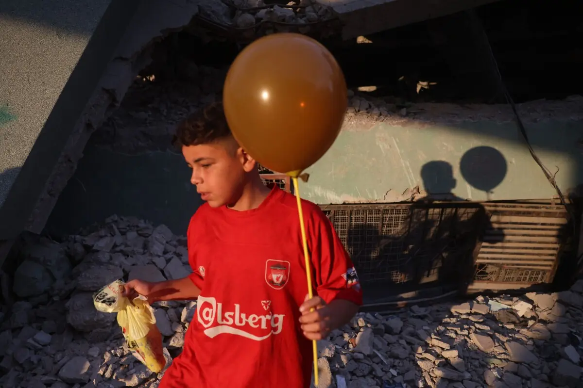 The shadow of a Palestinian boy holding a balloon is cast on the ruins of a destroyed building during morning prayers marking the start of Eidul Azha, in Khan Yunis in the southern Gaza Strip on May 27, 2026.