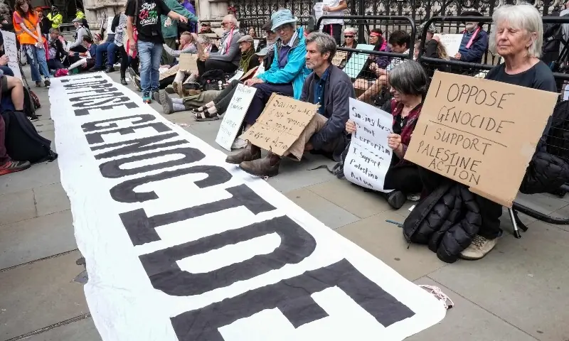 Protesters hold placards as they sit by a banner reading ‘I oppose genocide’, outside the Royal Courts Of Justice in central London on June 15, 2026, as the High Court rules on a legal standoff between the government and activist group Palestine Action. —AFP