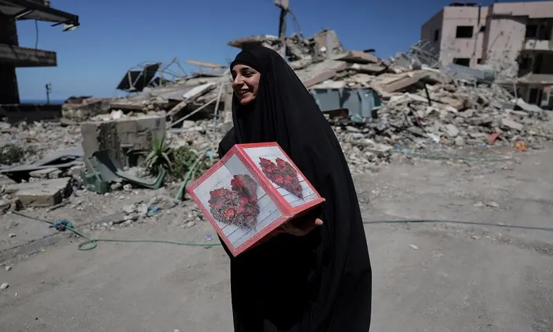 A woman returning to her village after displacement by the war smiles as she holds a box salvaged from her neighbour’s house, which was destroyed by an Israeli strike, in Qlaileh, Tyre district, southern Lebanon. — Reuters
