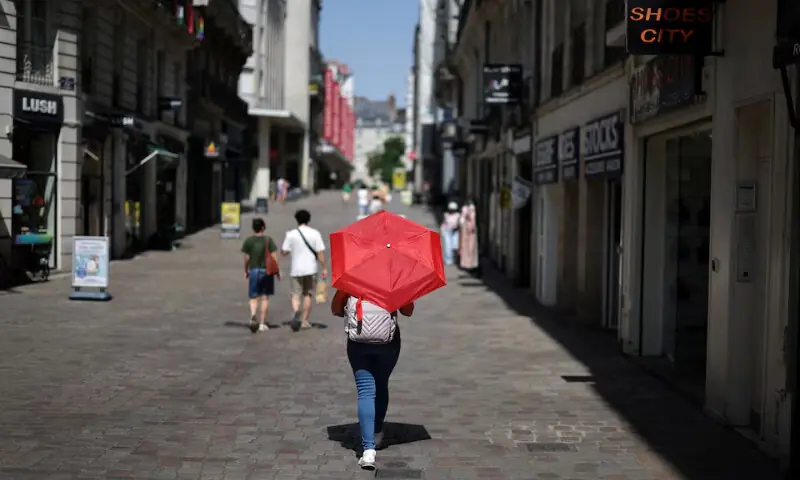 A woman uses a red umbrella to shade from the sun while walking on a street in Nantes as temperatures rise during a heatwave affecting a large part of France, June 22, 2026. — Reuters