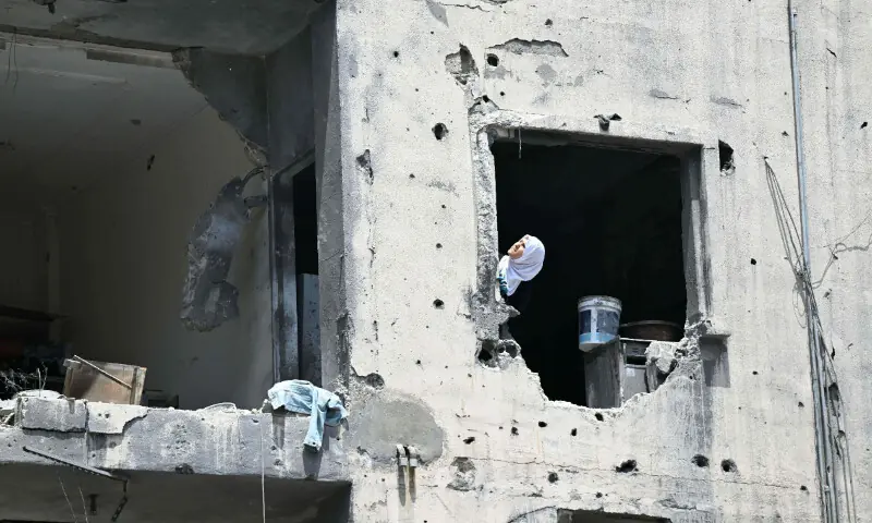  A woman looks up at construction workers as they removes debris from apartments in a damaged building at the site of an earlier Israeli military strike on a neighbourhood in the southern Lebanese coastal city of Tyre on June 23, 2026. &mdash; AFP 