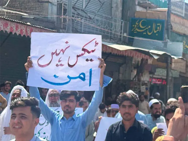 A man holds a placard during a protest in Khar, Bajaur, on Sunday. — Dawn